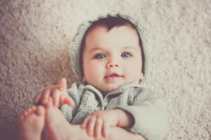 A cute baby in a knitted outfit lying on a soft carpet, smiling warmly.