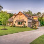 Elegant stone family home surrounded by trees, lush lawn, and vibrant garden.