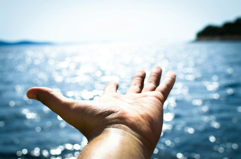 A hand reaching towards the sparkling sea, symbolizing freedom and hope.