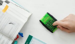 A student uses a green calculator to solve math equations from a textbook on a desk.