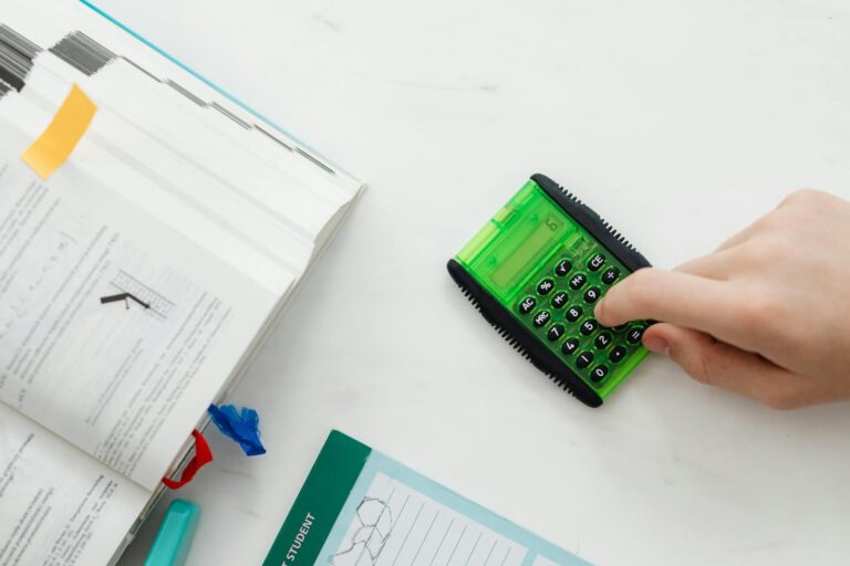 A student uses a green calculator to solve math equations from a textbook on a desk.