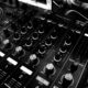 Black and white close-up of a DJ's audio mixing console with knobs and controls.