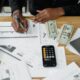 Man working on financial reports with calculator, money, and laptop on a desk.