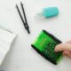 Close-up of a hand using a green calculator with stationery for studies or business calculations.