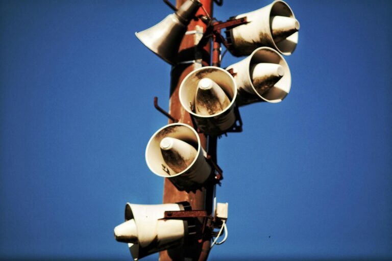 Cluster of outdoor loudspeakers mounted on a pole with clear blue sky in the background.