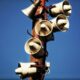 Cluster of outdoor loudspeakers mounted on a pole with clear blue sky in the background.