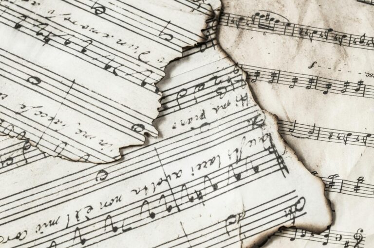 Close-up of aged, burnt music sheets displaying musical notes and compositions in detail.